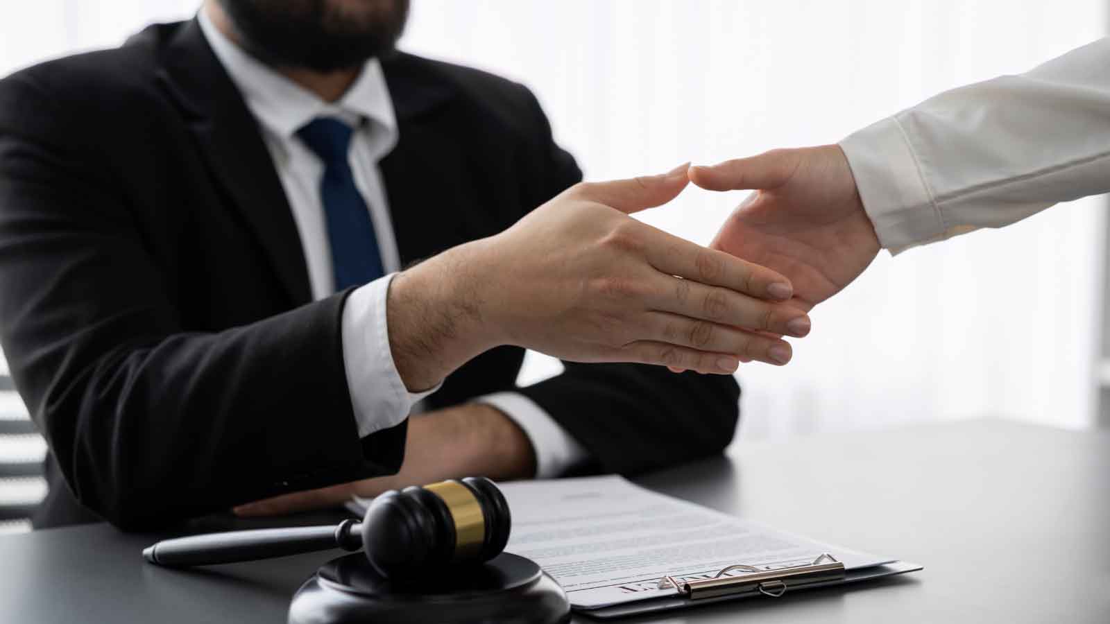 A handshake over a desk with legal papers and a gavel, signifying a legal agreement
