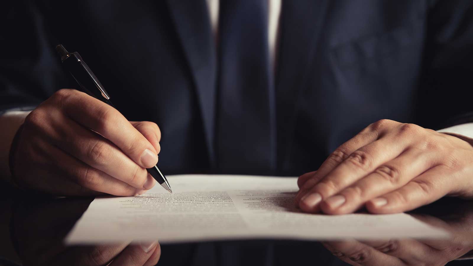 A person in a suit signing a document with a pen