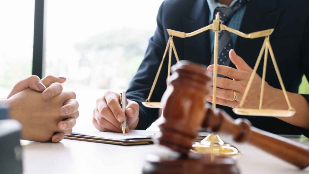 Two people in a discussion at a desk with a gavel and scales of justice in the foreground