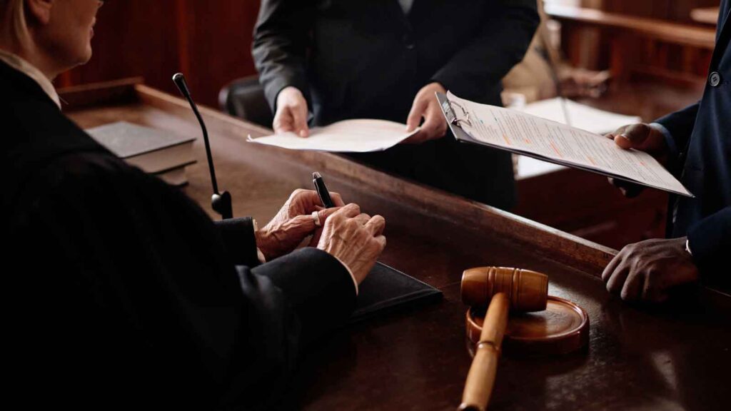 Judge signing a legal document in a courtroom with attorneys.