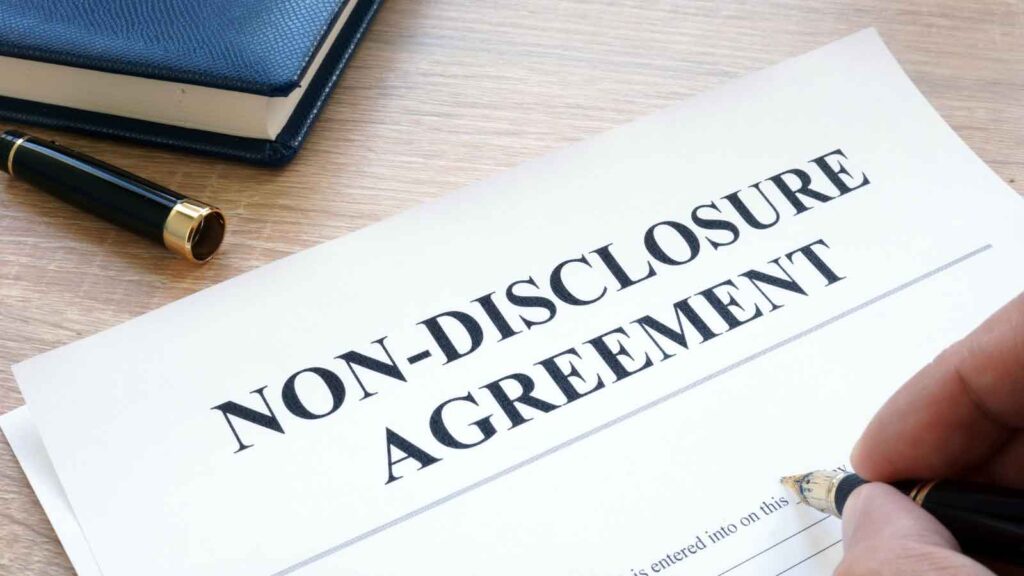 Person signing a non-disclosure agreement document on a desk.
