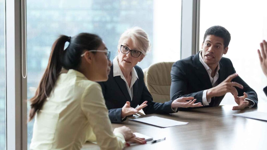 Three professionals in a tense business discussion at a conference table.