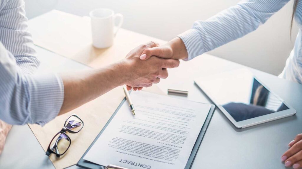 Two people shaking hands over a signed contract