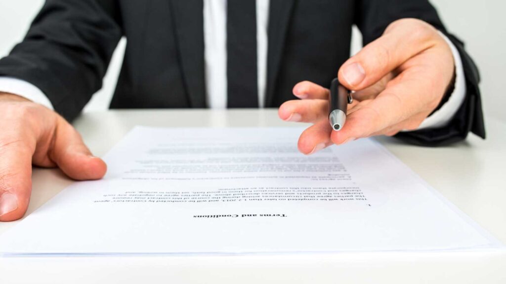 A person in a suit offers a pen to sign a contract.