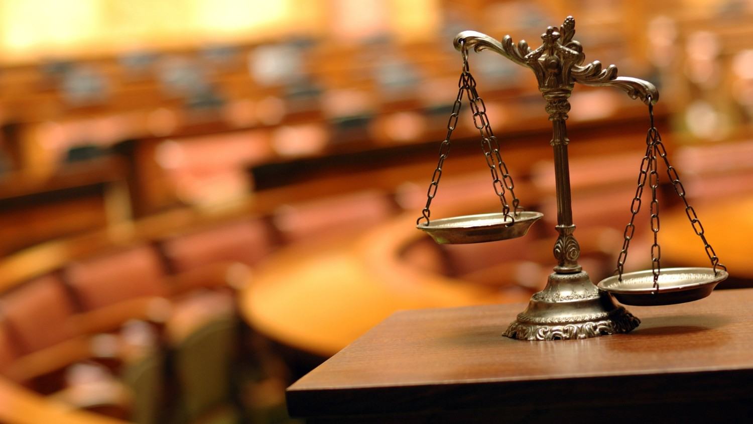Ornate brass scales of justice on a wooden bench inside a courtroom.